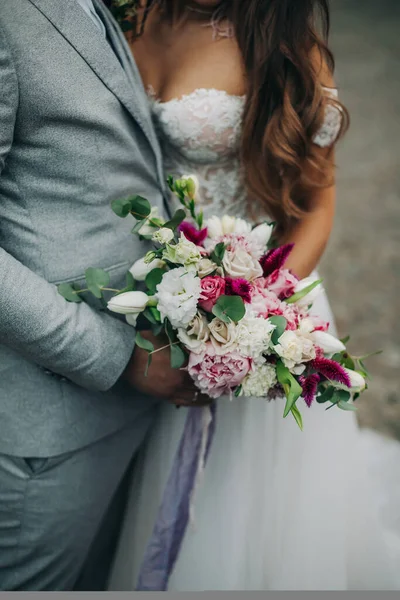 婚礼。穿西装的新郎和穿白衣的新娘肩并肩地站在一起，紧紧地拿着花束 — 图库照片