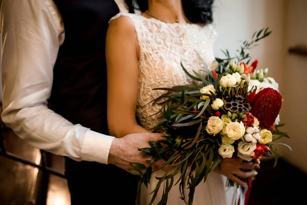 Ellerinde bir buket çiçek ve yeşillikle gelin ve damat kucaklaşır.