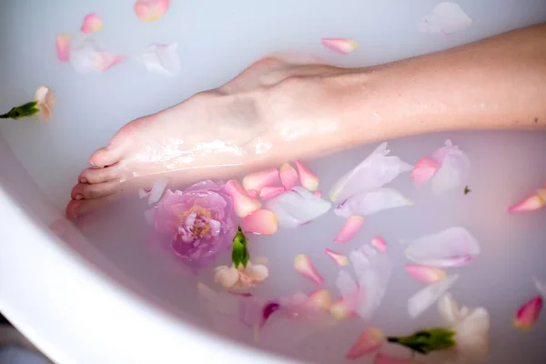 Um pé de meninas em uma banheira cheia de leite e pétalas de rosa.Relaxe, romance — Fotografia de Stock