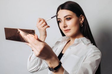 Aynada kendine makyaj yapan güzel bir kadının portresi, beyaz bir arka planda izole edilmiş..