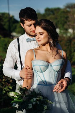 Bir gelin ve damat Paris 'teki düğün günlerinde Eyfel kulesinin önünde romantik bir an yaşıyor. Mavi gökyüzü, gelinin ellerinde düğün buketi, mavi gelinlik, sarılmalar