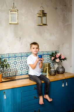 Tezgahta oturan ve ekmek yiyen bir çocuk. Mutfağın arka planında izole edilmiş. Çocuk boks kutusunu tutuyor.