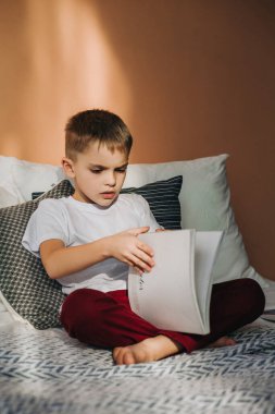 Küçük bir çocuk yatakta oturmuş bir dergiye bakıyor.