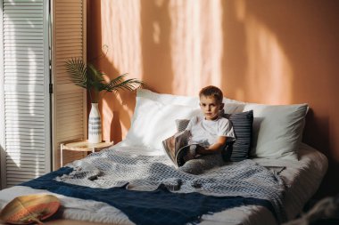 Küçük bir çocuk yatakta oturmuş bir dergiye bakıyor.