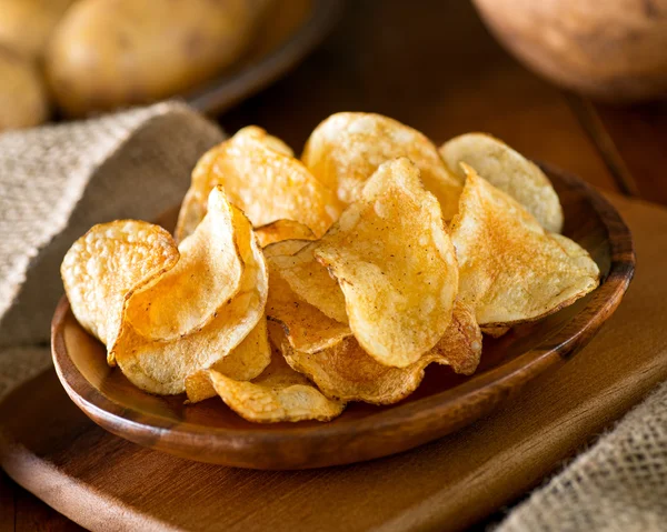 Köstliche hausgemachte Kartoffelchips mit Meersalz und schwarzem Pfeffer vor rustikalem Hintergrund. — Stockfoto