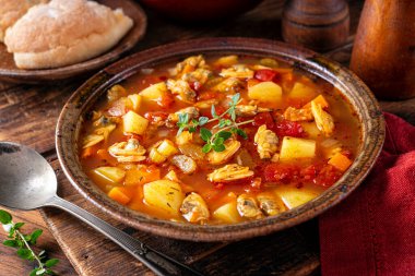 Bir kase lezzetli Manhattan midye çorbası ve ahşap bir masada taze kekik garnitürü..