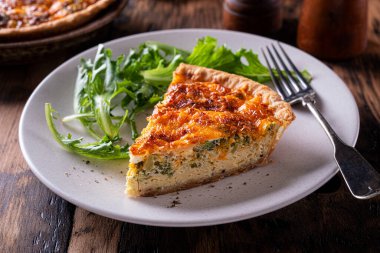 Bir dilim lezzetli brokoli ve ahşap bir masanın üstünde çedar keki..