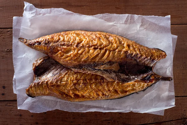 Smoked mackerel fillets on parchment paper against a rustic wooden background. — Stock Photo, Image