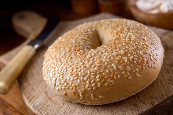 A delicious sesame seed bagel on a rustic wooden table top. — Stock Photo, Image