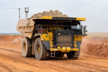 a mining dump truck drives and unloads bauxite minerals from the body into a warehouse against the background of the sky clipart