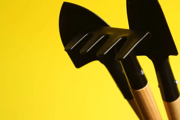 three small objects for working with soil and flowers on a yellow background, 2 shovels and rake