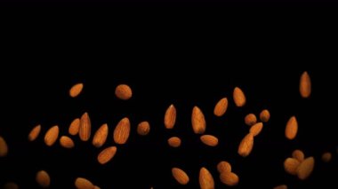 Siyah arka planda bir sürü badem cevizi uçurmak. Yiyecekler, sağlıklı yiyecekler, diyet. Badem dönüşünün 3 boyutlu animasyonu. Döngü canlandırması.