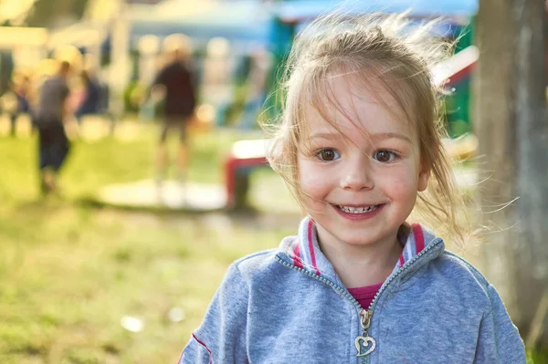 Adorable petite fille souriante dans le parc avec aire de jeux en arrière-plan — Photo