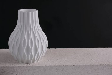 Koyu arkaplan, modern sanatsal işçiliğe karşı minimalist beton bir yüzeye yerleştirilmiş desenli üç boyutlu zarif beyaz vazo. Yüksek kalite fotoğraf