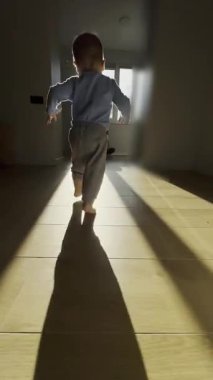 Çıplak bacaklı bir çocuk güneşli bir pencereden annesine doğru koşuyor. Kamera onun adımlarını takip ediyor, mutlu bir aile anını yakalıyor ve evdeki ilk adımlarını atıyor. Yüksek kalite 4k görüntü