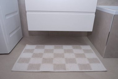 Banyo zeminindeki dama halısı sıcaklık yaratıyor. Yumuşak zemin paspası, bej ve beyaz fayanslar. İç tasarım, temiz ve modern banyo dekorasyonu. Ev için konfor ve tarz