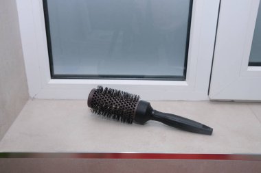 Yuvarlak bir saç fırçası pencere pervazında durur, güzellik rutinlerini ve özbakımını ima eder. Mekan, güzellik ve yaşam tarzı kavramları için ideal bir spa gününü çağrıştırıyor.