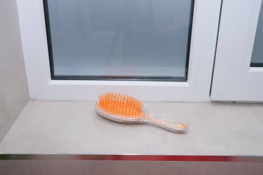 Saç fırçası banyodaki çıkıntıda oturup kullanılmayı bekliyor. Görüntü kişisel hijyen, kişisel bakım ve günlük rutinleri temsil ediyor. Güzellik, sağlık ve yaşam tarzı içeriği için ideal