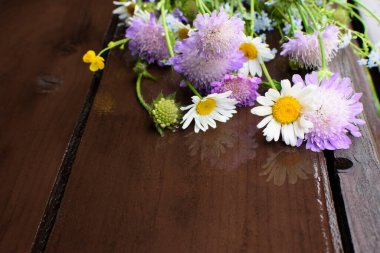 Romantic bouquet of wildflowers lying on the dark brown wooden table. Summertime. Copy space. Selective focus. 