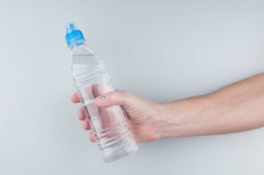 Gri arka planda elinde plastik bir şişe maden suyu tutuyordu.