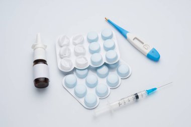 Mavi arka planda burun spreyi, şırınga, tablet ve termometre.