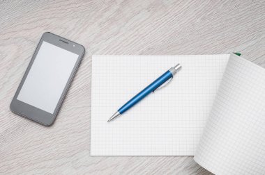 Ahşap arka planda cep telefonu, not defteri ve kalemle çalışan masa. Üst görünüm