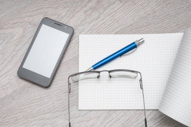 Akıllı telefon, not defteri ve tahta arka planda gözlüklü masaüstü