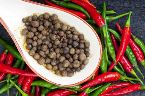 Hot peppers and peppercorns on wooden background — Stock Photo, Image