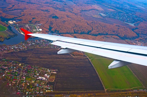 Wing of airplane flying above the fields — Stock Photo, Image