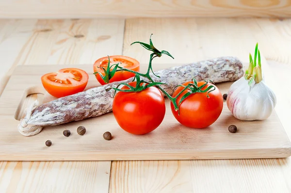 Smoked sausage with tomatoes and garlic on wooden board — Stock Photo, Image
