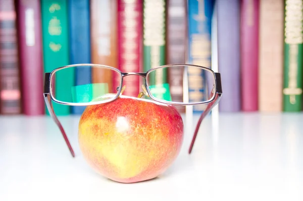 An apple with eyeglasses and colorful books on background — Stock Photo, Image