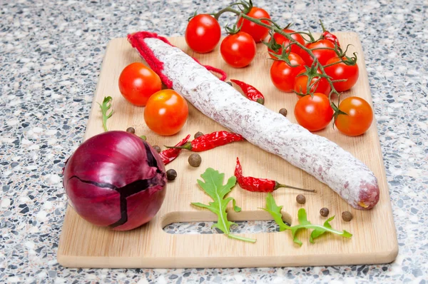 Smoked sausage, tomatoes and onion on a wooden board — Stock Photo, Image