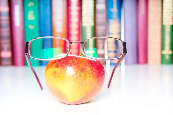 Ein Apfel mit Brille und bunten Büchern im Hintergrund — Stockfoto