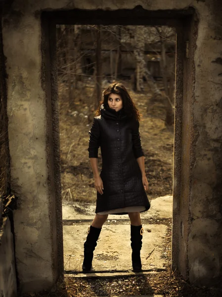 A brunette girl with black eyes with black hair in a black cloak is standing in the ruins of a wall — Stock Photo, Image