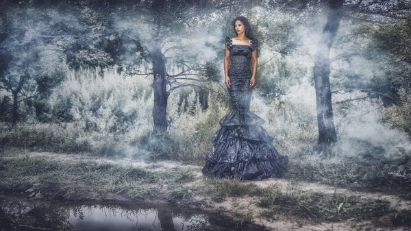 Girl in a very long dress. Walk down the path along the pond. Fog
