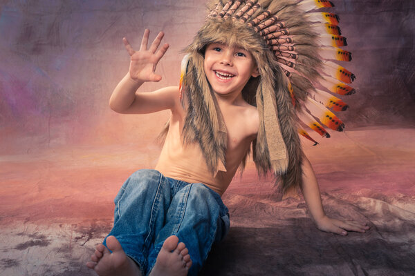 A little handsome boy laughs loudly, falls sits in a crown of American Indian feathers