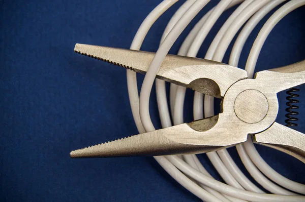 Wire cutters or diagonal pliers and white wires close up on dark blue backgroun