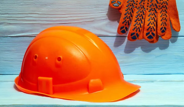 Construction orange helmet work gloves against the background of blue boards