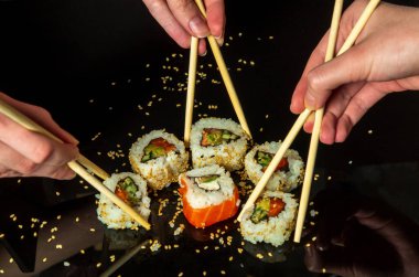 Kadınların elinde sopayla suşi rulosu olur. Siyah arka plan. Yaratıcı kavram