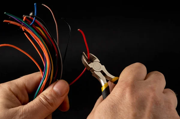 Hands of the master hold wire cutters and wire closeup on black background. Electronics Repair Ide