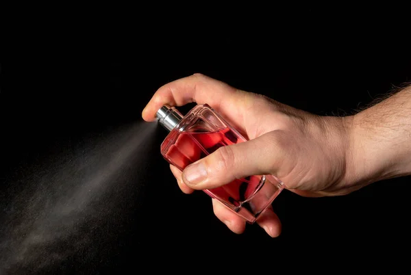 Hand man spraying perfume on black background close up