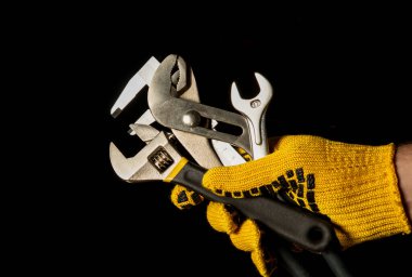 Ustanın iş eldivenindeki el, tesisatı tamir etmek için gerekli aletleri tutuyor.