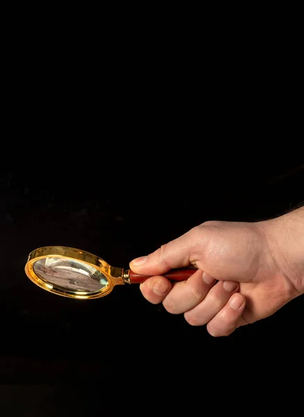 Man hand holding a gilded magnifying glass, close-up on black background. Copy space for your image or text