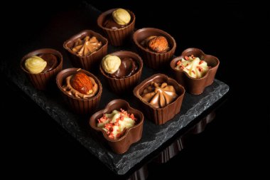 Kremalı ve fındıklı şeker. Siyah izole edilmiş arka planda çeşitli çikolatalar. Lokantada tatlı fikri