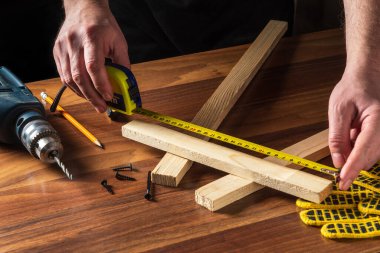 Marangoz ya da marangoz bir tahta parçasının uzunluğunu ölçmek için bir inşaat bandı kullanır. İşyerindeki ustanın elleri. Marangozluk atölyesinde çalışma ortamı