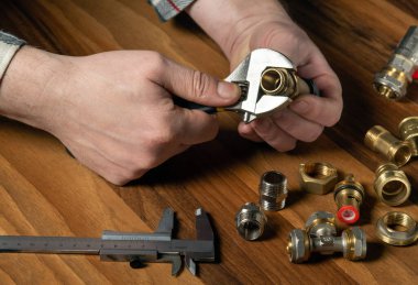 Tesisatçı, boru anahtarıyla vanaya pirinç vida takıyor. Efendinin elleri yakın plan