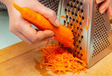 Kadınlar havucu rendeyle fırçalayan ellerdir. Sağlıklı yiyecekler, doğal, organik vejetaryen ürünler. Evde pişir.