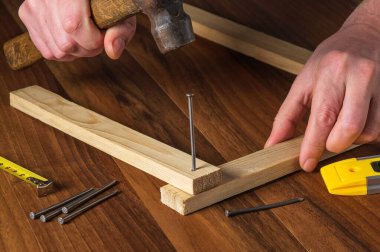 Ahşap işçisi çekiçle tahtaya çivi çakıyor. Ustanın elleri yakın plan. Marangozluk atölyesinde çalışma ortamı