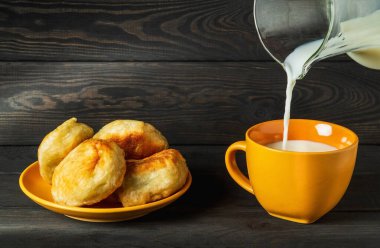 Süt testiden sarı bir kupaya dökülür. Lezzetli bir kahvaltı için fikir ya da sütle akşam yemeği ve ev yapımı çörekler.