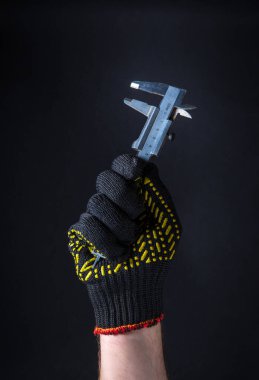 Eldivenli işçi koyu bir arka planda Caliper 'ı tutuyor. İnşa veya yenileme için fikir